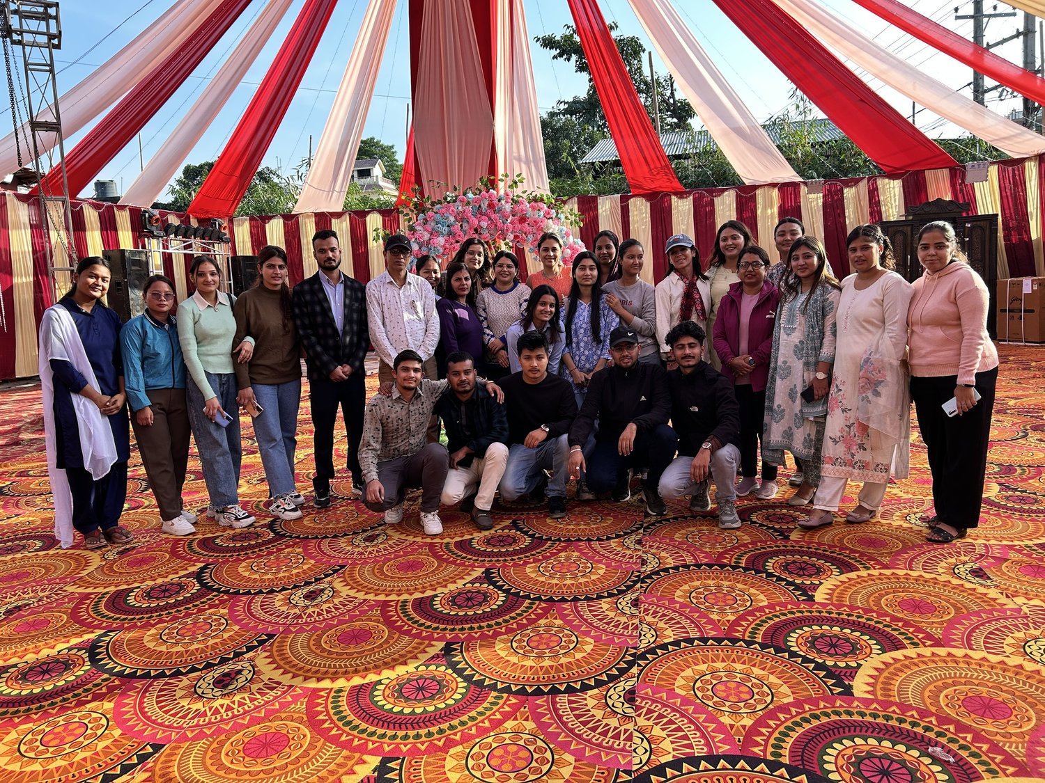 A large group of young women and men together under a red and white canopy at a program gathering