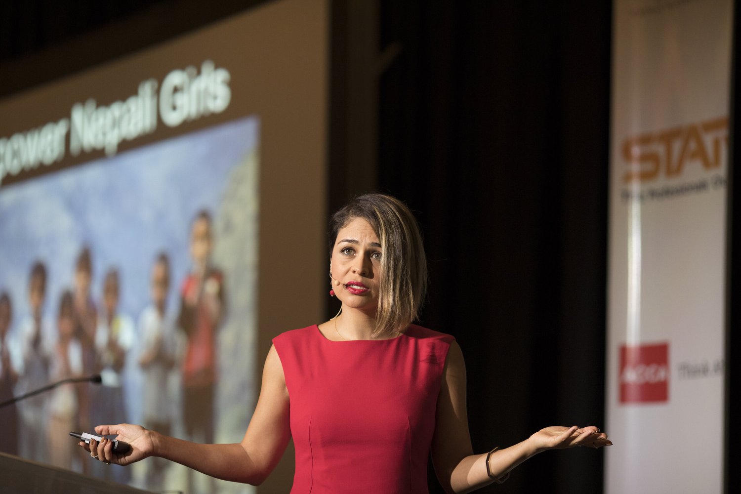 Dr. Sara Safari speaking on stage in front of a slide reading Empower Nepali Girls