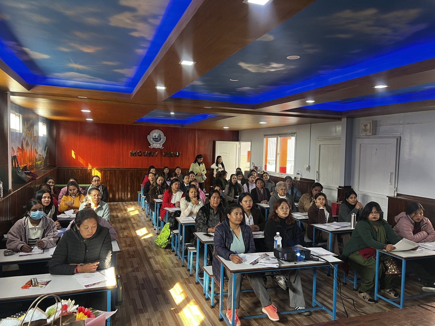 A room of women seated at desks during a leadership workshop, taking notes
