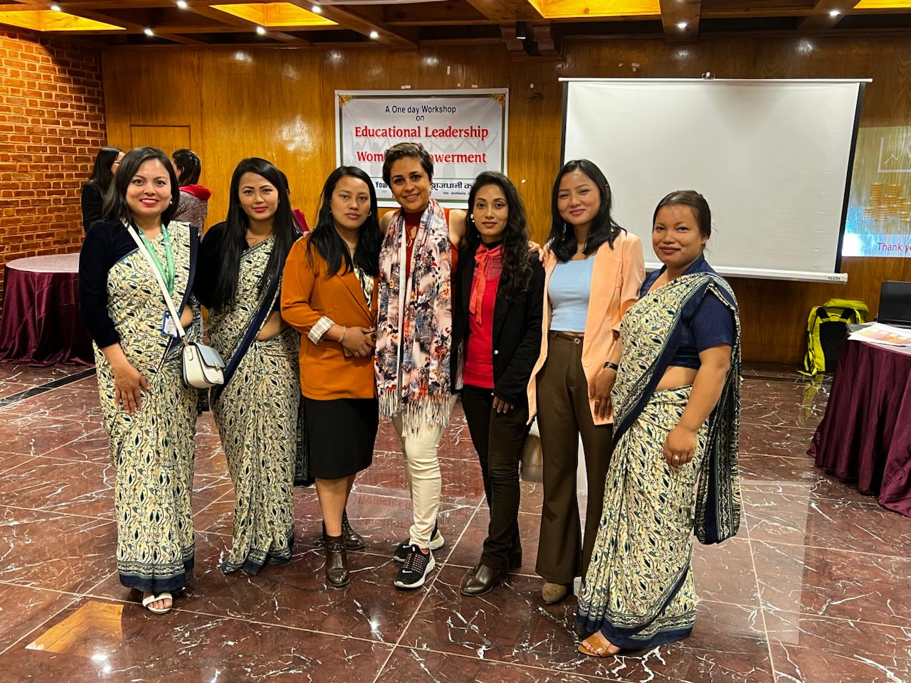 Seven women standing arm in arm in front of a banner for a one-day workshop on educational leadership and women's empowerment
